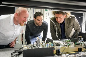Drei Männer in einem Labor schauen gemeinsam auf eine technische Konstruktion