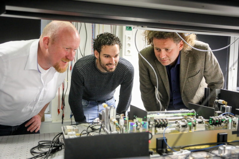 Drei Männer in einem Labor schauen gemeinsam auf eine technische Konstruktion