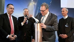 Vier Männer stehen zusammen; einer fügt das Modell einer Rakete in einen Zylinder ein