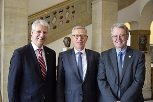 Drei Männer schauen in die Kamera; im Hintergrund das Treppenhaus des Bremer Rathaus