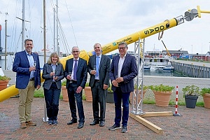 Fünf Personen stehen mit einem Glas Sekt in der Hand vor einer Tonne