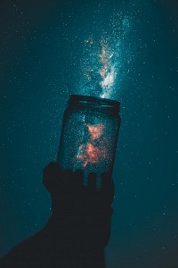 Ein leeres Schraubglas wird in den Nachthimmel gehalten; man sieht leuchtende Teilchen aus dem Glas entströmen