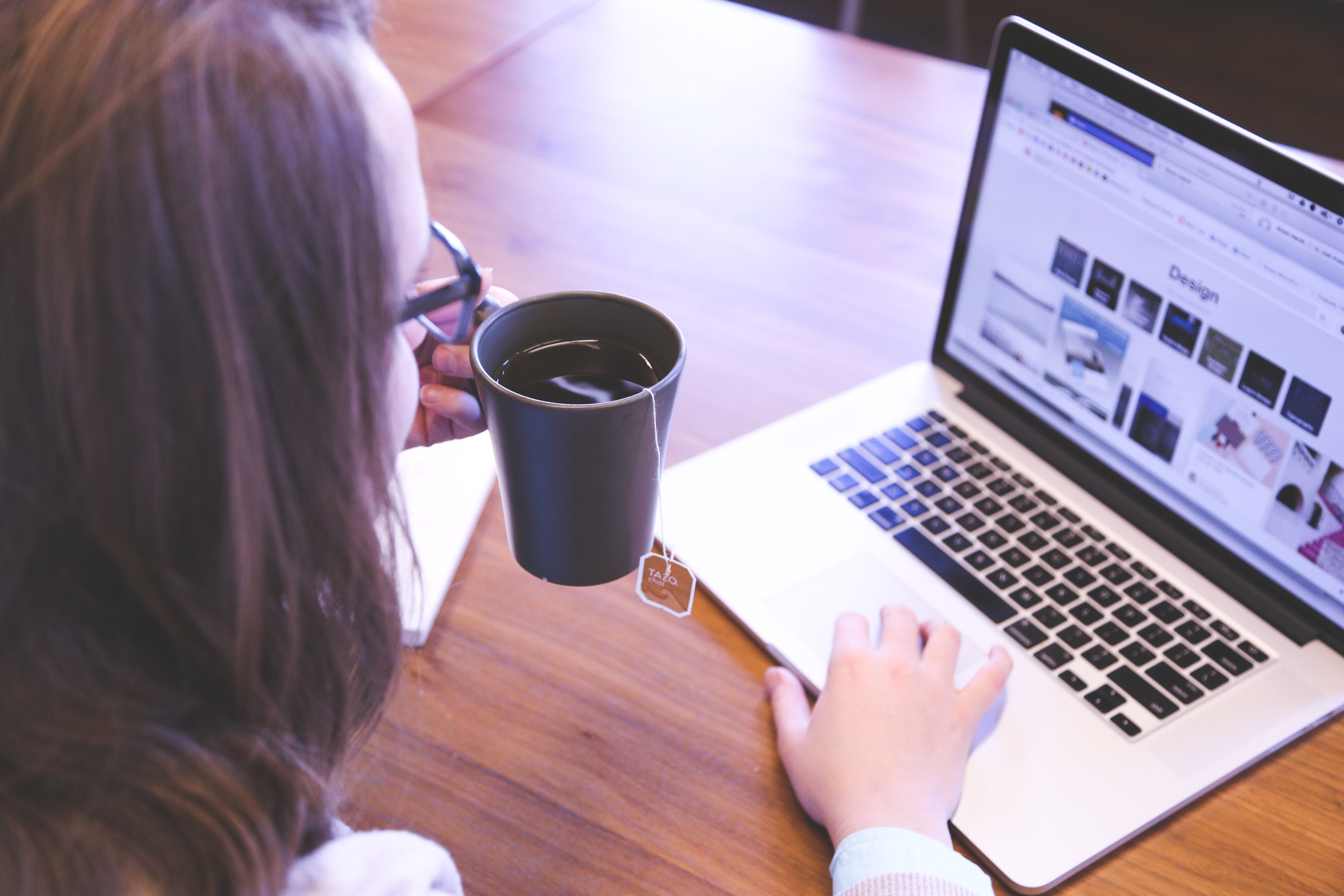 Eine Frau hält eine Teetasse und schaut auf ihren Laptop