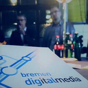 Zwei Männer stehen an einem Tisch mit Getränken und es ist ein Plakat zu sehen, auf dem bremen digitalmedia steht