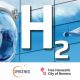 Ein Kopf im Astronautenhelm vor einer blauen Glaswand; Schriftzug: H2