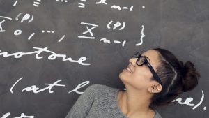 Frau schaut auf eine Matheformel an der Tafel hinter sich