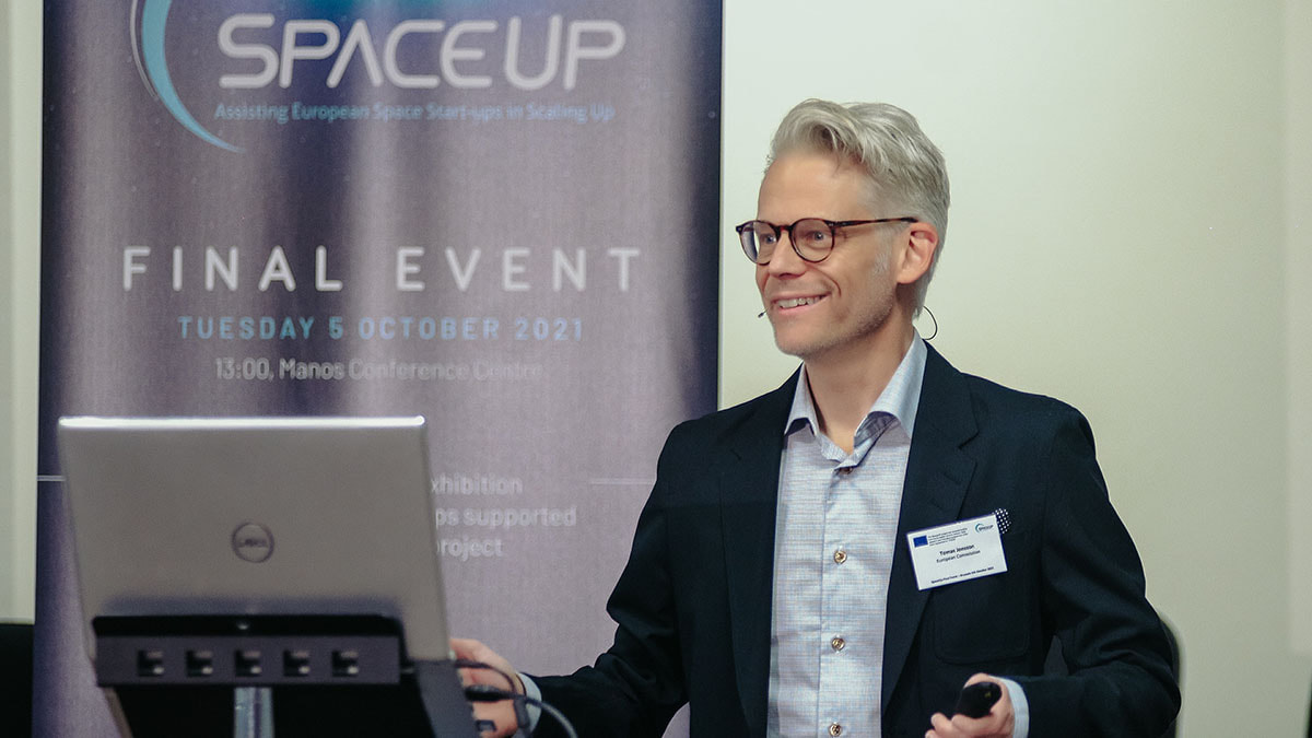 Ein Mann steht mit Mikrofon vor einem Laptop und lächelt, im Hintergrund hängt ein Plakat vom Final Event von Space Up